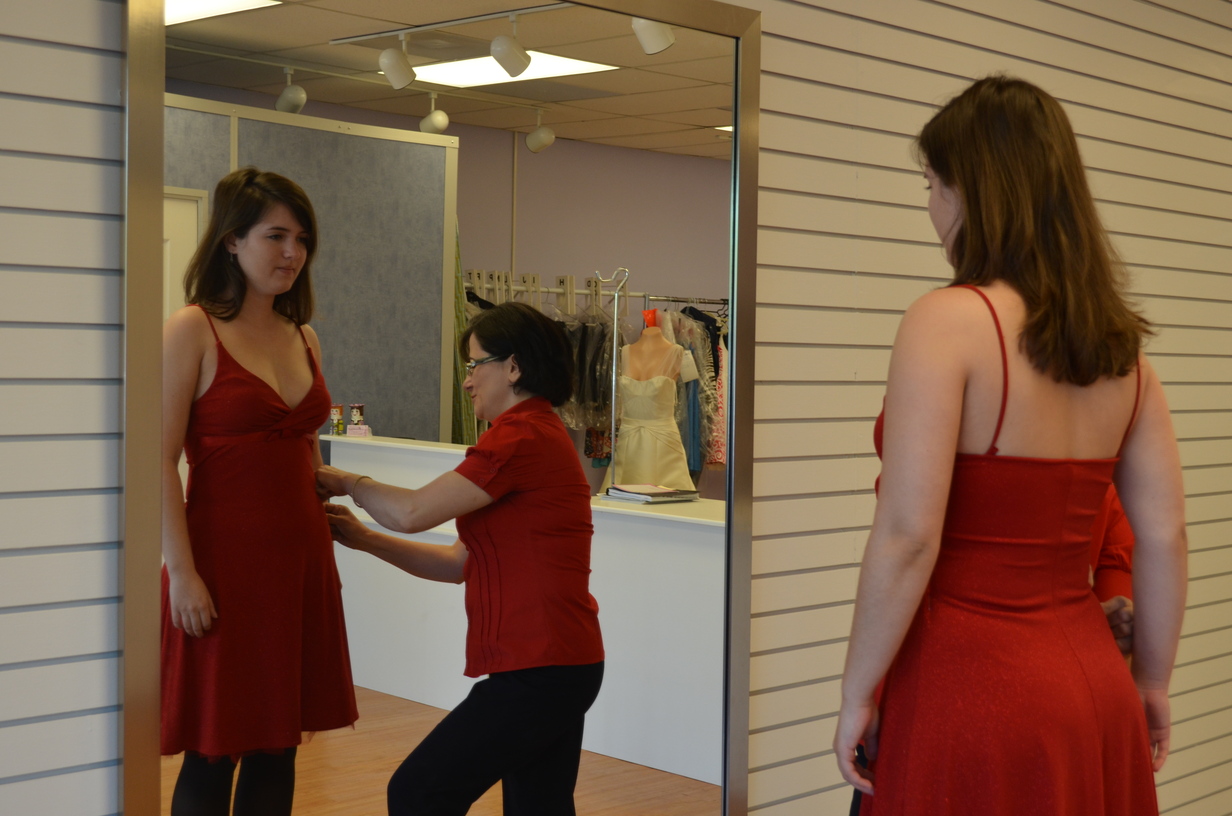 Mahnaz making measurements of a young woman in a red dress.